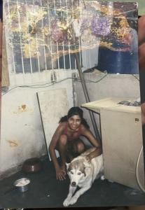 Registro de Patrícia aos 15 anos de idade, realizado na casa de sua tia, em São Paulo. Conhecida como Narizinho, ela aparece ainda adolescente ao lado de um cachorrinho da família. A fotografia revela um momento de intimidade cotidiana em um espaço doméstico.