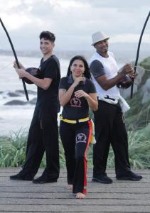 Fotografia de Patrícia ao lado do filho Kadu e do esposo Cláudio em um evento de capoeira. A imagem registra o núcleo familiar reunido, em um momento de convivência cotidiana, com os três posicionados próximos, evidenciando a relação entre mãe, pai (de consideração) e o filho.