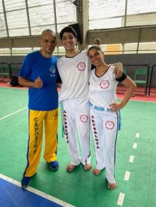 Patrícia aparece ao lado do filho Carlos Eduardo e de outro mestre de capoeira durante um evento realizado no bairro Jardim Nova República. Na imagem estão Mestre Tabu, o monitor Kadu, seu filho, e Patrícia, reunidos em um momento de encontro e prática da capoeira.