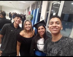 Registro da formatura de Patrícia no curso de Educação Física, em Cubatão, realizada entre 2018 e 2019. Na selfie aparecem seu filho Kadu, a professora Alessandra, Patrícia e Alephi, a quem ela considera filho do coração. A imagem mostra os formandos e acompanhantes usando beca, celebrando a conclusão do curso em um momento coletivo e afetivo.