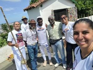 Patrícia aparece ao lado de mestres importantes da capoeira durante a subida ao Monte Serrat, em Santos, no ano de 2024. A imagem foi registrada em um evento em homenagem ao Mestre Bahia e reúne grandes nomes da capoeira, entre eles Mestre Sombra e Mestre Angoleiro. O grupo participa da caminhada como parte da celebração, marcando presença coletiva em um gesto simbólico de respeito e reconhecimento.
