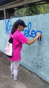 Registro de Patrícia grafitando durante uma atividade do Projeto da Linha Pra Frente, patrocinado pela Rumo, na Vila Esperança. A fotografia mostra Narizinho no uso do spray e a intervenção direta no muro, destacando sua participação ativa na ação artística.