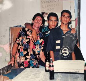 Nesta imagem, Tigrão, esposo de Dona Cícera, aparece ao lado dos filhos Patrique e Plínio durante uma comemoração de aniversário no Bar do Forró, espaço emblemático da Vila Esperança nos anos 1980 e 1990, conhecido por abrigar festas e forrós memoráveis. O registro destaca o laço entre pai e filhos, revelando um momento de afeto e união familiar em meio à efervescência cultural do bairro. A imagem também remete à atuação de Tigrão como figura ativa na vida comunitária e na construção de espaços de convivência.