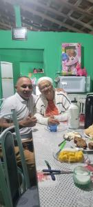 Registro de Alfredo e sua mãe, Dona Zefa, na cozinha do sítio onde ela reside, em João Alfredo, Pernambuco. O ambiente doméstico, com alimentos dispostos, remete à cultura alimentar nordestina que atravessa gerações. A imagem evidencia como os saberes culinários aprendidos nesse espaço familiar acompanham Alfredo ao longo da vida e se manifestam também em seu cotidiano na Vila Esperança, em Cubatão, onde esses sabores são recriados e compartilhados no Cabeça’s Bar. A fotografia conecta memória, afeto e tradição por meio da comida.