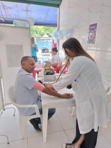 A fotografia mostra Alfredo participando ativamente da ação de saúde realizada em seu bar, enquanto uma agente de saúde afere sua pressão arterial. Ao se colocar também como usuário do serviço, Alfredo reforça a importância do cuidado preventivo e do acesso coletivo à saúde. O gesto evidencia uma liderança baseada no exemplo e na proximidade com os moradores da Vila Esperança, fortalecendo a confiança da comunidade nas ações realizadas naquele espaço improvisado, porém essencial.