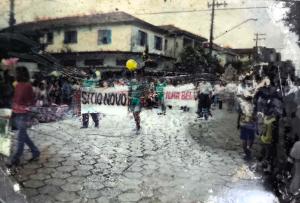 A imagem registra um desfile que apresentava os bairros da Vila Esperança durante um evento oficial na cidade de Cubatão, no início dos anos 2000. Moradores carregam faixas com o nome de cada localidade, afirmando identidade, pertencimento e reivindicando reconhecimento público para suas comunidades.
