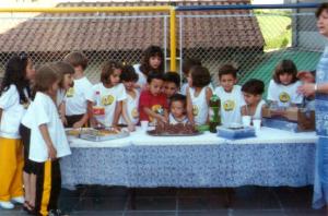 Primeira festa de aniversário do Vitor na escola. Na foto, Vitor está de camiseta vermelha e cortando o bolo.