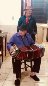 O avô, José, e o pai de Ivandro, vestidos a gaúcha, tocando Bandoneón. Ivandro conta que os dois são muito importantes pra ele, sempre sorriem e tocam músicas, tornando o dia de todos mais leve. O primeiro instrumento que Ivandro teve, um violão, veio do avô. A música é a essência família, sempre tocam quando estão juntos.