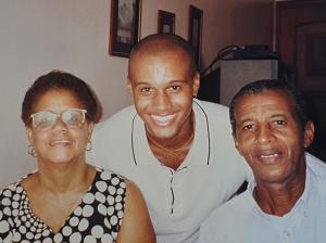 : Sorridentes, Alexon, aos 24 anos, com os pais, Daniel e Eunice, na casa deles no bairro da Abolição, zona norte do Rio de Janeiro. Essa fotografia foi uma das últimas tiradas com sua mãe, que faleceu no ano seguinte.