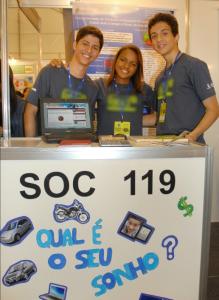 Primeira feira de ciências de Bia Santos fora do Rio de Janeiro, em 2013. O evento aconteceu dentro da Universidade de São Paulo e Bia apresentou o projeto de educação financeira feito no Ensino Médio, que deu origem a Barkus. Ao seu lado, estão os colegas Wallace e Marden, que atualmente é seu sócio.