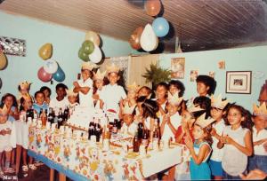 Milca durante sua primeira festa de aniversário, aos 5 anos, em São Félix do Xingu, no Pará, em 1986. Ela conta que, na época, festas de aniversário eram muito caras e era muito difícil fazerem na família. Recorda que foi um momento muito importante, pois estava muito feliz com sua festa. Na fotografia, muitas das crianças são filhas de pessoas da igreja da qual a família de Milca frequentava na época.