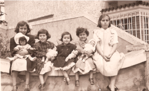 Márcia e suas irmãs sentadas no muro de sua casa no bairro do Ipiranga, durante a infância. Márcia conta que provavelmente Isabel estava emburrada de ter que se sentar no muro, todas, exceto ela, carregavam uma boneca no colo.