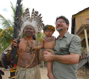 Binho Marques em visita à comunidade indígena, ao lado do cacique Bira Brasil, segurando no colo um dos filhos da liderança indígena. O registro simboliza a proximidade e o diálogo construídos com os povos da floresta ao longo de sua trajetória pública.
