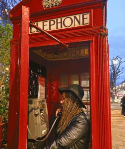 Juliane em uma cabine telefônica em Londres, na Inglaterra. Ela conta que sempre quis viajar sozinha, mas sua mãe sempre teve muito medo. Em abril de 2022, realizou o sonho de visitar a Europa pela primeira vez, sozinha e celebrando um novo momento de sua vida. Quando chegou na capital inglesa, primeiramente, sentiu medo, depois, empoderamento e animação. Fez amigos durante a viagem e durante um jantar, próximo ao Museu de História Natural, com uma amiga lituana, quis fotografar algo que representasse a realização desse momento, a cabine vermelha.