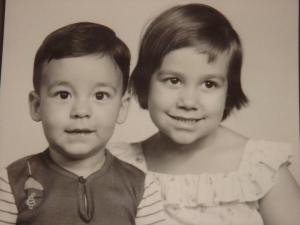 Guilherme e sua irmã, Carol, durante a infância, em uma sessão de fotografias em estúdio. A fotografia é um pôster e está pendurada na sala da casa da sala da mãe de Guilherme. Ele relembra que a camisa de lã que vestia tinha um fio solto no pescoço que sempre o incomodava, é uma das primeiras memórias de sua infância.