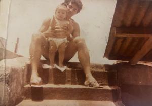 Dayana nos braços do pai sobre a laje da casa da família no Jardim Ingá, na Zona Sul de São Paulo. A cena entre pai e filha revela intimidade, cuidado e a construção dos primeiros vínculos afetivos em um território periférico da cidade.