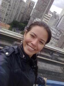 Dayana aparece com os prédios do centro ao fundo, durante o período em que trabalhava na região. A imagem reflete o ritmo urbano e a relação entre trabalho, cidade e identidade.