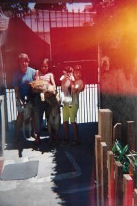 Christiane, entre oito e nove anos de idade, aparece ao lado de sua mãe, Eliane, e de sua irmã, Andrea, no quintal da casa onde viviam. A cena é compartilhada com as cachorrinhas da família: Quica, Nega e Xuxa, evidenciando um cotidiano marcado pela convivência afetiva entre pessoas e animais.