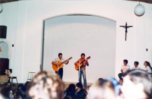 Dois rapazes tocam violão em um palco diante de uma multidão.