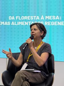 Cláudia Visoni durante uma palestra em Brasília, falando ao microfone sobre sistemas alimentares regenerativos.