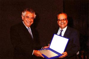 Juvenal recebendo homenagem pelos 30 anos de serviços prestados ao SENAC das mãos do Sr. Abram Szajman (Presidente da FCESP e do SENAC). Juvenal foi orador da turma.