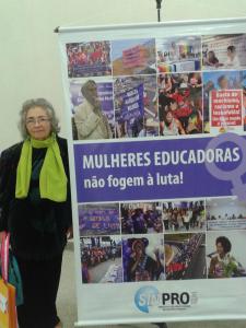Professora Holanda presente em Congresso, ao lado do cartaz “Mulheres Educadoras não fogem à luta!”