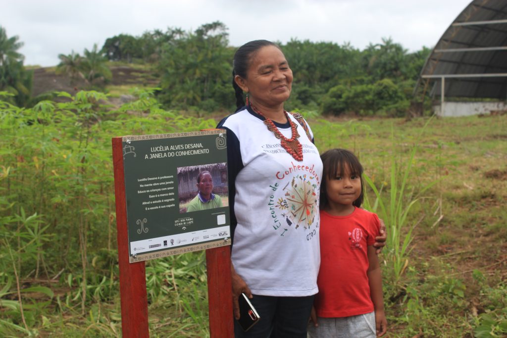 Dona Lucélia posando pra foto ao lado da placa em sua homenagem